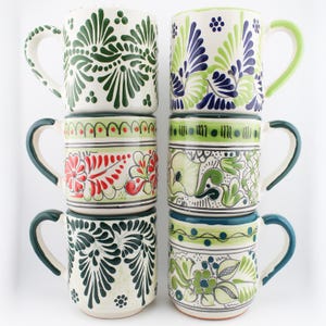 May include: Six ceramic mugs arranged in two vertical columns. Each mug features a unique hand-painted design with floral and leaf motifs in various colors including green, blue, red, and black on a cream-colored background with curved handles.
