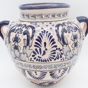 May include: A ceramic vase with two handles, featuring a cream-colored base and intricate blue floral patterns. The rim and handles are a deep blue, with additional gray accents. The vase has a rounded shape.