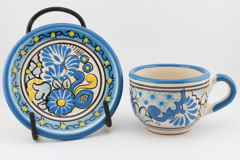 May include: A blue and white ceramic teacup and saucer set with a floral design. The cup has a handle and the saucer has a scalloped edge.