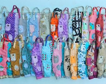Puede incluir: Una colección de petos coloridos y estampados con diversos diseños, incluyendo lunares, rayas y estampados florales. Cada peto tiene un bolsillo y un asa. Los petos se exhiben sobre un fondo azul claro.