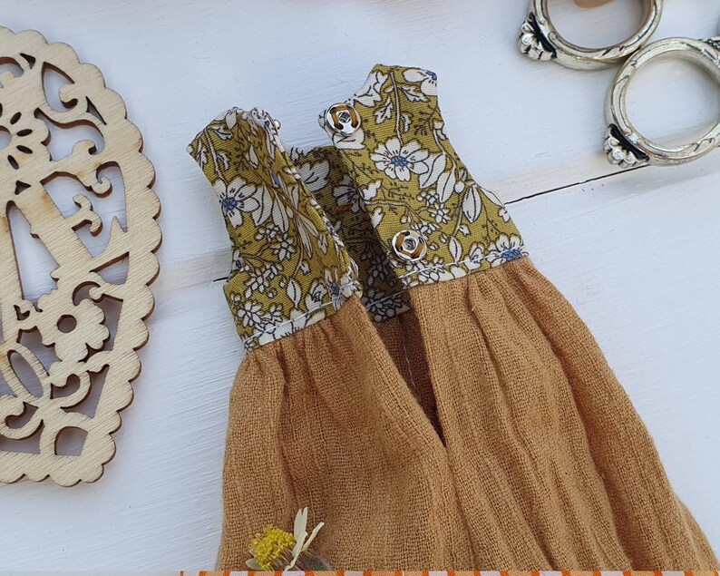 May include: A yellow and white floral print fabric doll dress with a mustard yellow skirt.
