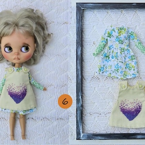 Puede incluir: Una mu&ntilde;eca con cabello rubio ondulado viste un vestido sin mangas amarillo claro con un gr&aacute;fico de coraz&oacute;n morado sobre una camisa de manga larga con estampado floral verde y blanco, junto a un conjunto a juego dentro de un marco negro.