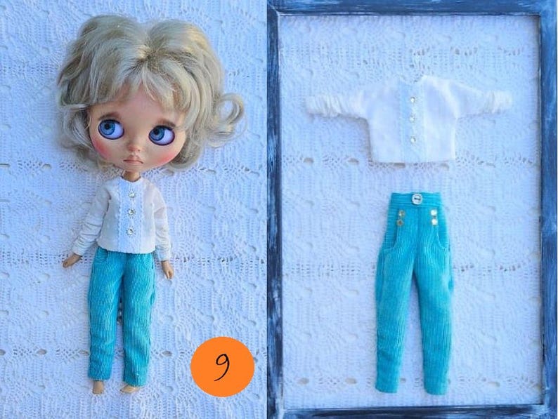 Puede incluir: Una mu&ntilde;eca con cabello rubio ondulado y grandes ojos azules que viste una blusa blanca de manga larga con tres botones y pantalones turquesa. Al lado hay una blusa blanca a juego y pantalones turquesa con un bot&oacute;n y detalles dorados.