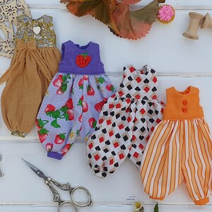 May include: Four handmade doll dresses in different patterns and colors. The dresses are made of cotton fabric and have a variety of details, including ruffles, buttons, and embroidery.