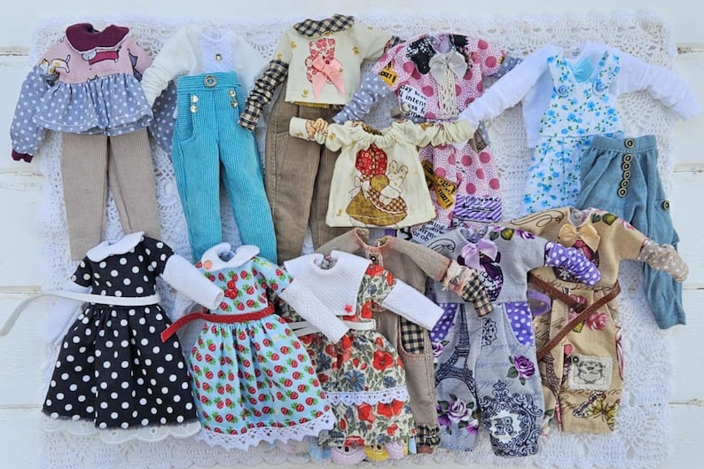Puede incluir: Una colecci&oacute;n de ropa de mu&ntilde;eca en miniatura que incluye varios tops, pantalones, vestidos y petos con diversos estampados como lunares, fresas, motivos florales y la Torre Eiffel en una amplia gama de colores y texturas de tela.