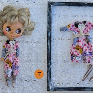 Puede incluir: Una mu&ntilde;eca de cabello rubio ondulado y ojos grandes viste un mono rosa de lunares con detalles de estampado de peri&oacute;dico, un lazo blanco y calcetines a rayas. Junto a ella, un mono y calcetines a juego se exhiben en un marco negro.