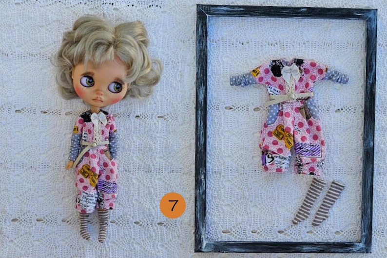 Puede incluir: Una mu&ntilde;eca de cabello rubio ondulado y ojos grandes viste un mono rosa de lunares con detalles de estampado de peri&oacute;dico, un lazo blanco y calcetines a rayas. Junto a ella, un mono y calcetines a juego se exhiben en un marco negro.