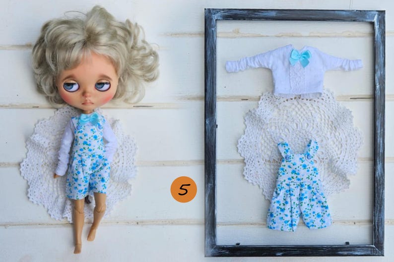 Puede incluir: Una mu&ntilde;eca de cabello rubio viste una camisa blanca de manga larga y un overol azul con estampado floral y un lazo azul claro. Al lado, un conjunto enmarcado incluye una camisa blanca de manga larga con un lazo azul claro y un overol floral a juego.