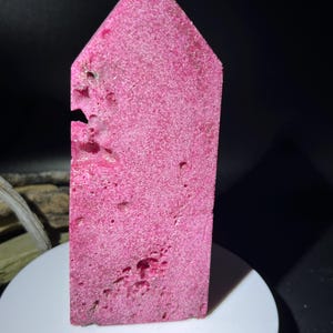 May include: A pink, rough-textured, pointed crystal with a natural, irregular shape. The crystal is a natural, raw, and unpolished specimen.
