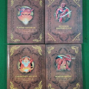 Puede incluir: Cuatro libros de Advanced Dungeons & Dragons con cubiertas marrones y bordes dorados. Los títulos incluyen "Players Handbook", "Dungeon Masters Guide", "Unearthed Arcana" y "Monster Manual". Cada libro presenta una ilustración de criatura fantástica.