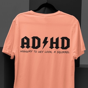 May include: A peach colored t-shirt with a black graphic that says "AD/HD HIGHWAY TO HEY LOOK, A SQUIRREL"
