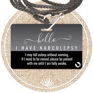 May include: A black and gray badge with the text "hello I HAVE NARCOLEPSY". The badge includes a warning about falling asleep without warning and a request for patience. It has a black lanyard and a silver clasp.