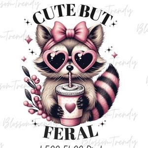 May include: Cute but feral graphic featuring a cartoon raccoon wearing pink sunglasses and a pink bow. The raccoon is holding a pink and white cup with a straw and a pink heart design. The text "Cute but Feral" is written below the raccoon.
