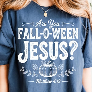 May include: A navy blue t-shirt with the text "Are You FALL-O-WEEN JESUS?" in white. A white pumpkin and leaf design is below the text, with "Matthew 4:19" underneath. The shirt is a casual, short-sleeved style.