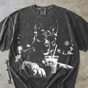 May include: Dark gray t-shirt featuring a black and white graphic of a dog wearing sunglasses and holding a drink with a straw. The drink cup has the text "NO COPY". The shirt has a vintage, distressed look.