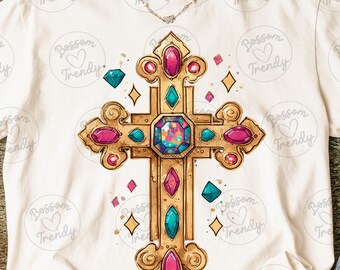 Peut inclure: T-shirt crème avec un motif de croix dorée ornée de pierres précieuses roses, turquoise et bleues. La croix est centrée sur le t-shirt, avec un collier délicat visible. Le t-shirt porte l'inscription "Bossom Trendy".