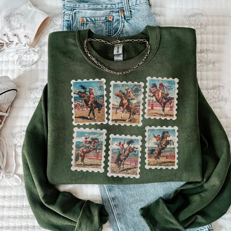 Op de afbeelding: Een donkergroene sweatshirt met zes postzegelontwerpen met rodeo-sc&egrave;nes. De postzegels tonen cowboys op wilde paarden. Een gouden ketting ligt op de sweatshirt. De sweatshirt wordt gecombineerd met een blauwe jeans en witte sneakers.
