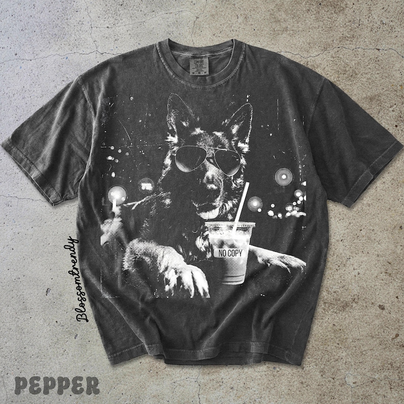 May include: Dark gray t-shirt featuring a black and white graphic of a dog wearing sunglasses and holding a drink with a straw. The drink cup has the text "NO COPY". The shirt has a vintage, distressed look.