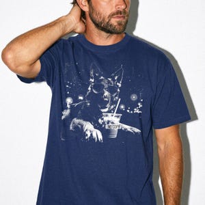 May include: Navy blue t-shirt featuring a black and white graphic of a German Shepherd wearing sunglasses and holding a drink. The drink cup has the text "NO COPY". The shirt is a short-sleeved crew neck.