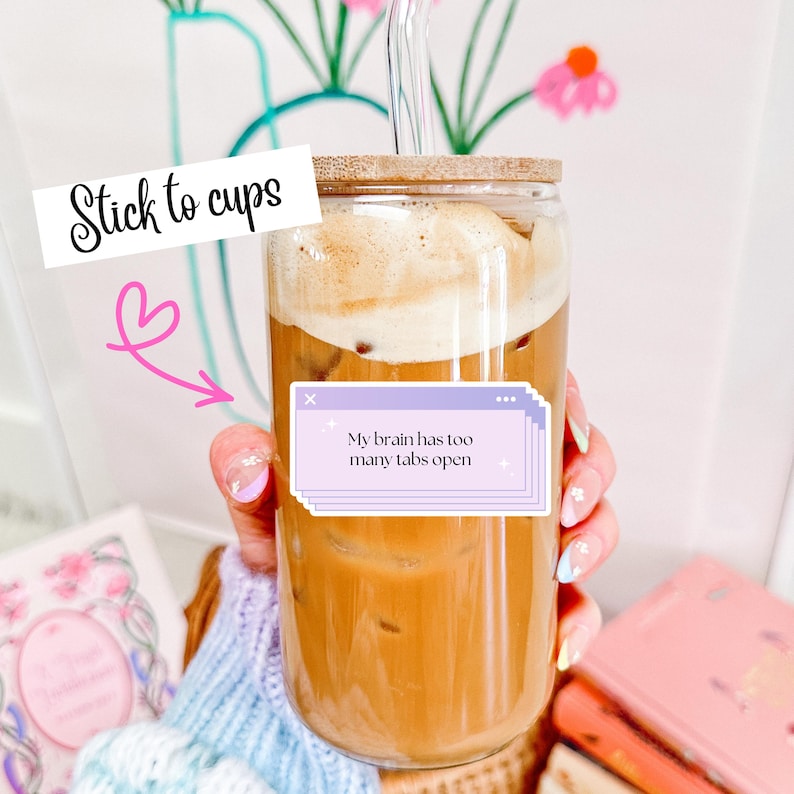 May include: A clear glass cup filled with a light brown beverage and topped with foam. The cup has a bamboo lid and a glass straw. Text on the cup reads "My brain has too many tabs open" and "Stick to cups".