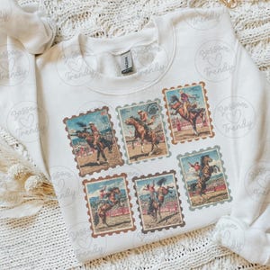 Op de afbeelding: Witte sweatshirt met zes vintage postzegelontwerpen met rodeo-sc&egrave;nes. Elke postzegel toont een cowboy op een bucking bronco of paard, met een bruine rand en een verweerde uitstraling.