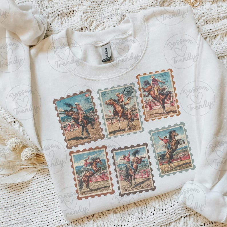 Op de afbeelding: Witte sweatshirt met zes vintage postzegelontwerpen met rodeo-sc&egrave;nes. Elke postzegel toont een cowboy op een bucking bronco of paard, met een bruine rand en een verweerde uitstraling.