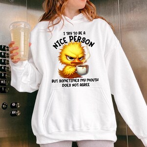 Pu&ograve; includere: Felpa bianca con un cartone animato di un pulcino giallo che tiene una tazza di caff&egrave;. Il testo sulla felpa recita "Cerco di essere una persona gentile, ma a volte la mia bocca non &egrave; d'accordo."