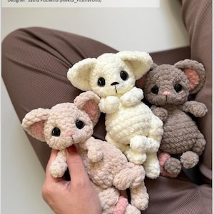 May include: Three crocheted plush toys: a cream-coloured mouse, a light brown mouse, and a grey mouse. The toys have large black eyes, pink accents, and are made from a soft, textured yarn. The text "Crochet Pattern 'Mini Mouse and Fennec Fox'" is visible.