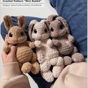以下が含まれることがあります： 茶色とベージュの色合いの、かぎ針編みのミニウサギのぬいぐるみ3つ。ウサギは大きな黒い目と鼻と足にピンクのアクセントがあります。画像上部には「Crochet Pattern 'Mini Rabbit'」の文字が見えます。