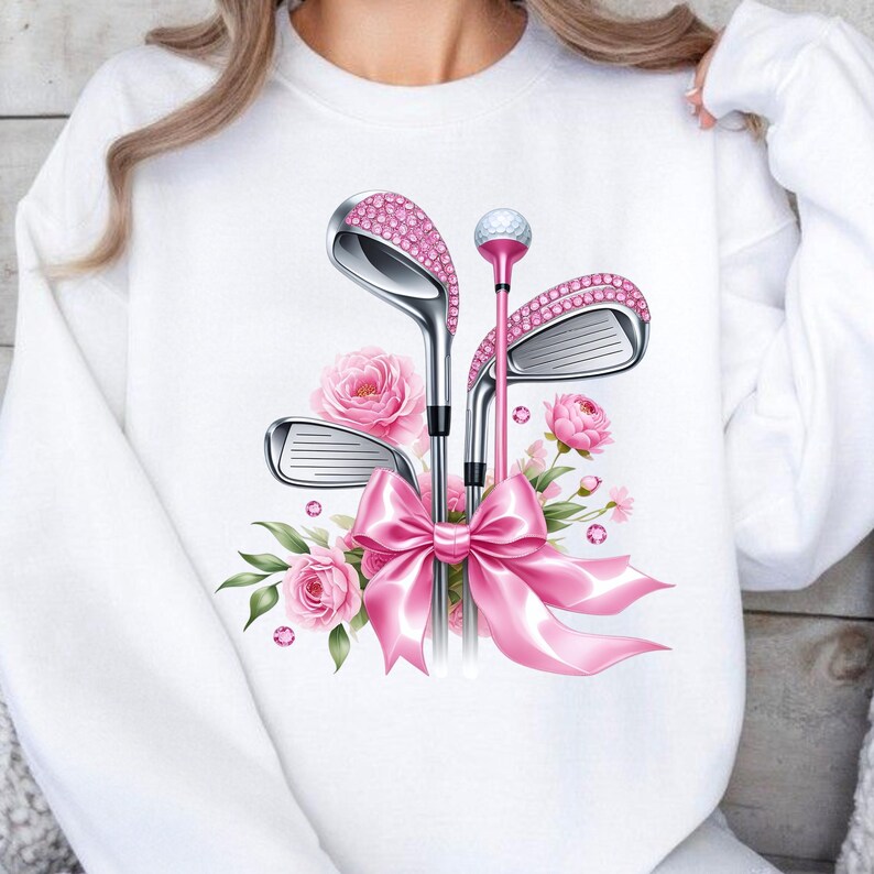 May include: White sweatshirt with a pink floral design and pink golf clubs with rhinestones. The clubs are tied together with a pink bow.
