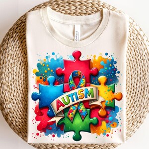May include: A white t-shirt with a colorful design of puzzle pieces and a ribbon with the word "AUTISM" on it. The design is surrounded by colorful paint splatters.