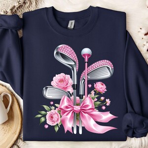 May include: Navy blue sweatshirt with a pink floral design and a set of golf clubs with pink accents. The clubs are adorned with rhinestones.