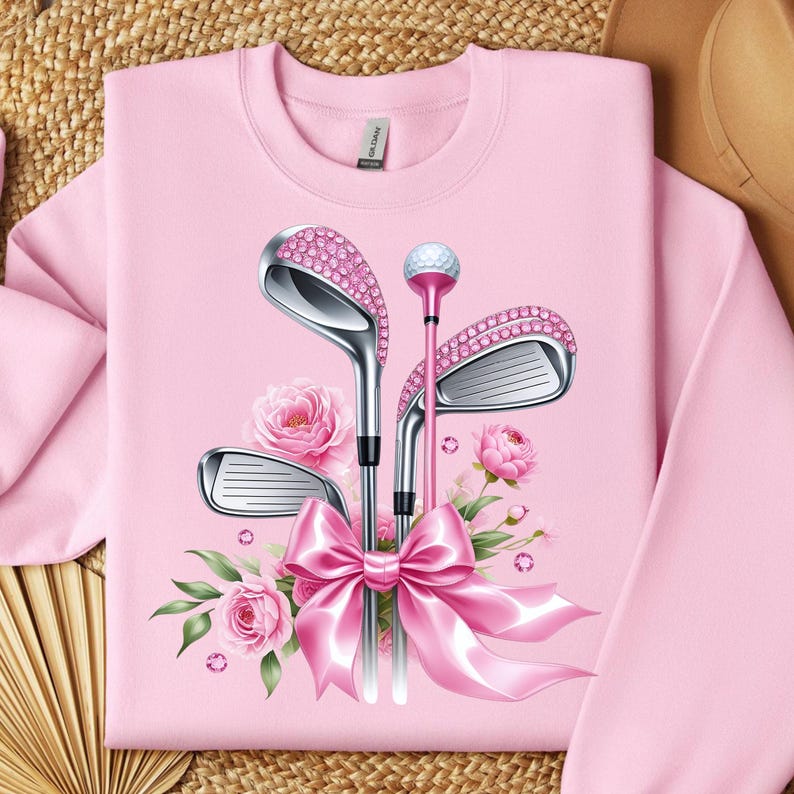 May include: Pink sweatshirt with a graphic of pink golf clubs with rhinestones and a pink bow.