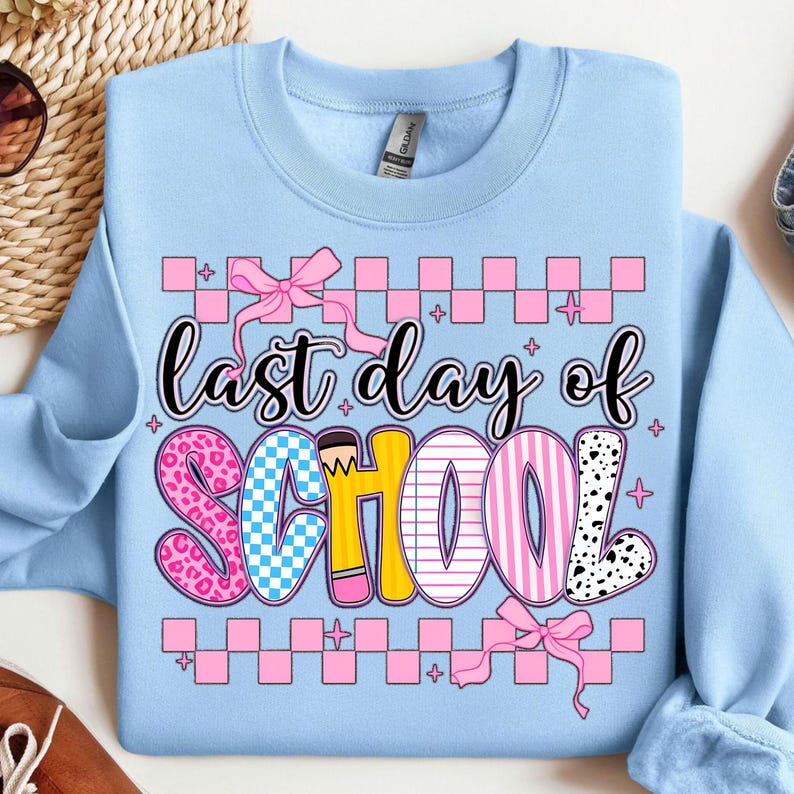 Puede incluir: Sudadera azul claro con el texto "&uacute;ltimo d&iacute;a de escuela" en letras rosas, amarillas, azules y negras. Las letras est&aacute;n decoradas con patrones de cuadros, rayas y lunares. El texto est&aacute; rodeado por un borde de cuadros rosa y blanco.