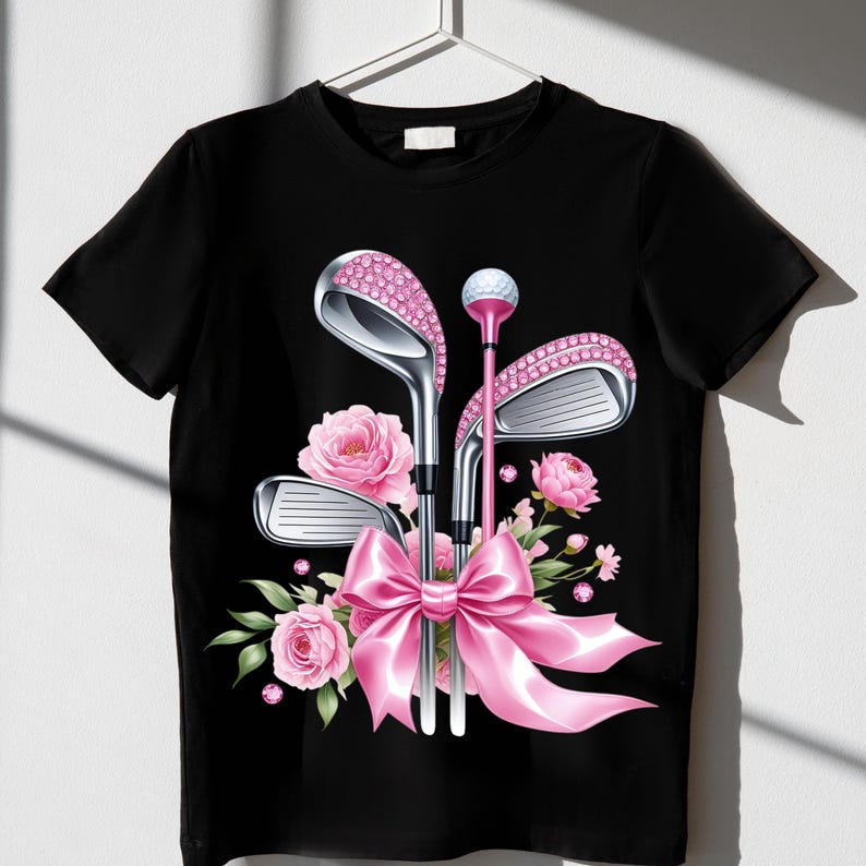 May include: Black t-shirt with a pink bow and three golf clubs with pink rhinestones. The clubs are surrounded by pink flowers.