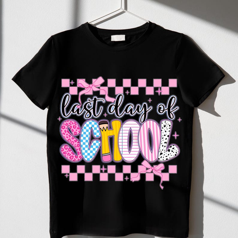Puede incluir: Camiseta negra con un patr&oacute;n de cuadros rosa y blanco, un lazo rosa y el texto "&uacute;ltimo d&iacute;a de escuela" en letras de colores con un gr&aacute;fico de l&aacute;piz.