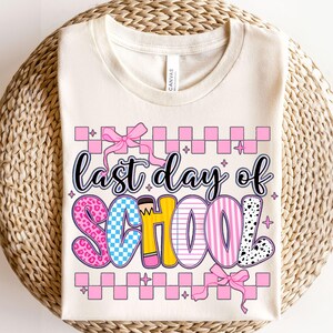 Puede incluir: Una camiseta beige con el texto "&uacute;ltimo d&iacute;a de escuela" en letras de colores con un patr&oacute;n de cuadros rosas y lazos rosas.