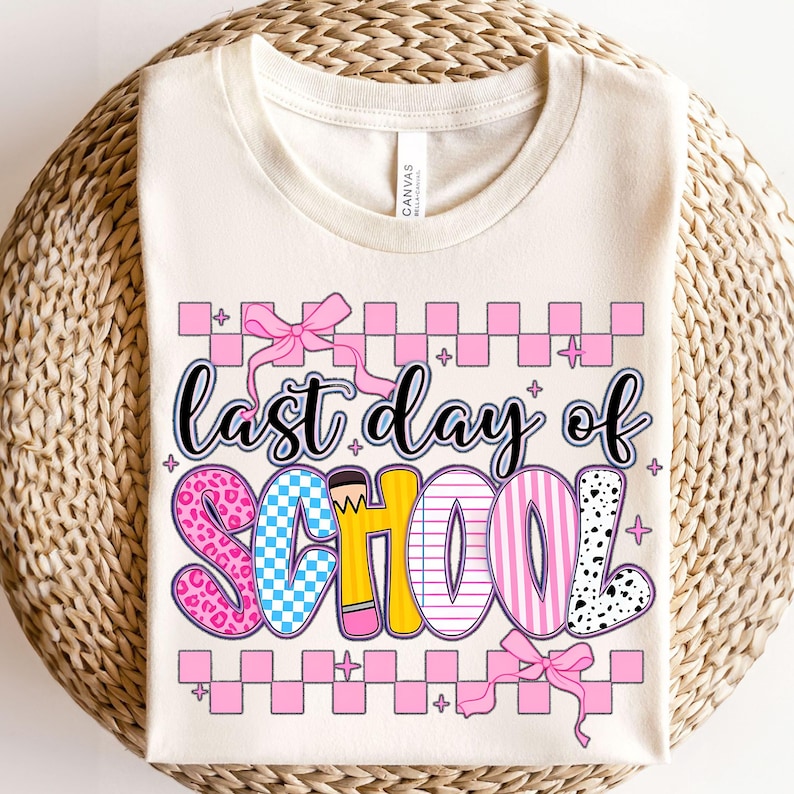Puede incluir: Una camiseta beige con el texto "&uacute;ltimo d&iacute;a de escuela" en letras de colores con un patr&oacute;n de cuadros rosas y lazos rosas.