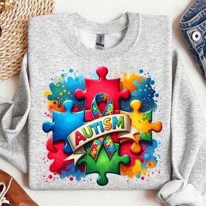 May include: A gray sweatshirt with a colorful design of puzzle pieces and a ribbon. The text "AUTISM" is written on a banner.