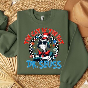 Peut inclure: Sweat-shirt vert avec un motif du Chat dans le Chapeau portant un casque et un n&oelig;ud papillon rouge. Le texte "The Cat in the Hat" est dans un cercle blanc avec une bordure &agrave; carreaux noir et blanc. Le texte "Dr. Seuss" est en bleu sous le motif.