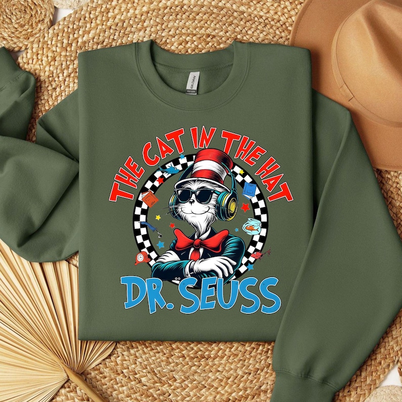Peut inclure: Sweat-shirt vert avec un motif du Chat dans le Chapeau portant un casque et un n&oelig;ud papillon rouge. Le texte "The Cat in the Hat" est dans un cercle blanc avec une bordure &agrave; carreaux noir et blanc. Le texte "Dr. Seuss" est en bleu sous le motif.