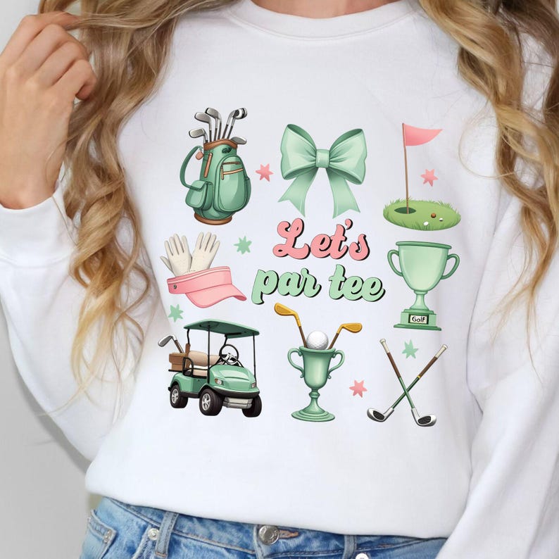 May include: White sweatshirt with a green and pink golf-themed design. It features a golf bag, golf clubs, a golf cart, a trophy, a golf ball, a pink bow, a pink visor, and the text "Let's par tee".