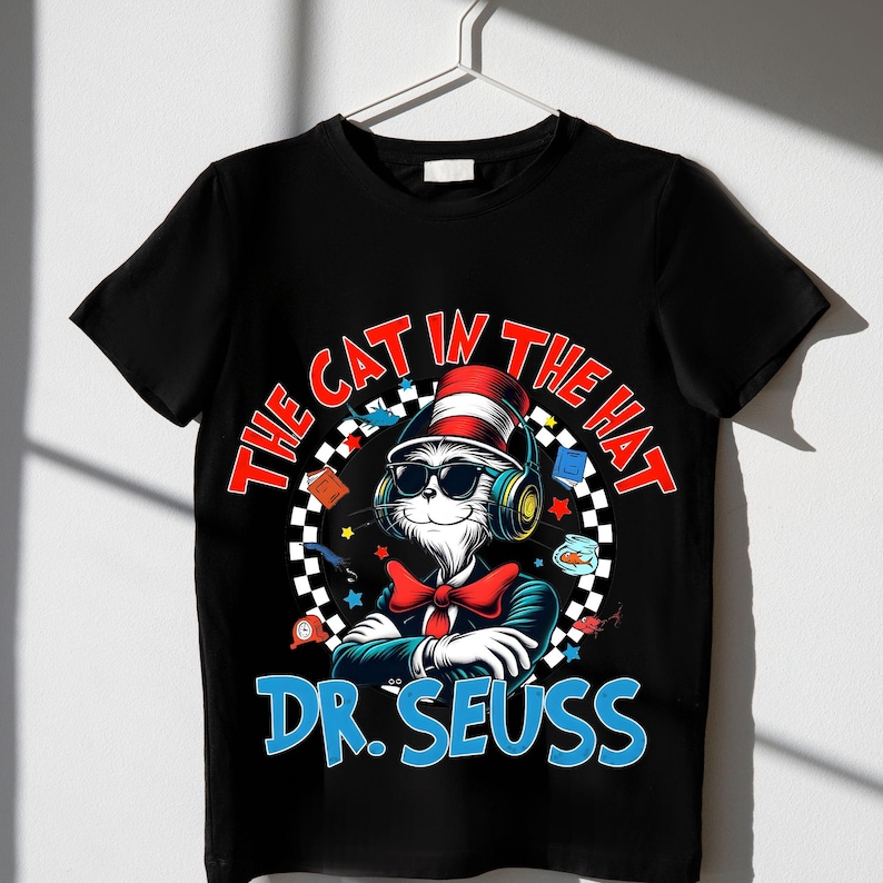 Peut inclure: T-shirt noir avec un graphique circulaire blanc repr&eacute;sentant un chat de dessin anim&eacute; portant un chapeau rouge et blanc, des lunettes de soleil et un casque. Le texte "THE CAT IN THE HAT" est &eacute;crit en arc rouge et blanc autour du chat. Le texte "DR. SEUSS" est &eacute;crit en bleu sous le chat.