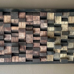 May include: A rectangular wall art piece made of wood blocks in various shades of brown, black, and natural wood. The blocks are arranged in a random pattern, creating a textured and visually interesting design.