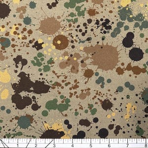 May include: A fabric with a tan background covered in paint splatters in shades of brown, green, yellow, and black. The splatters vary in size and shape, creating a textured pattern.