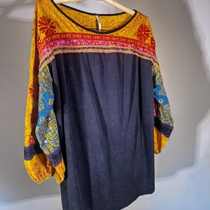 Puede incluir: Una camisa de manga larga con estampado azul y amarillo, con un cuerpo azul oscuro y un ribete colorido alrededor del escote.