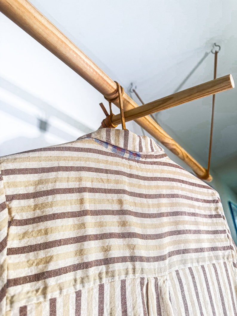 Op de afbeelding: Een gestreept shirt hangt aan een houten kledingrek. Het shirt is een lichtbruin en wit gestreept patroon.