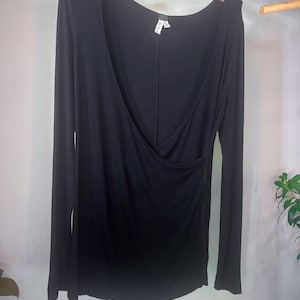 Puede incluir: Una camisa negra de manga larga con cuello en V profundo y dise&ntilde;o de envoltura. La camisa est&aacute; hecha de una tela suave y el&aacute;stica.