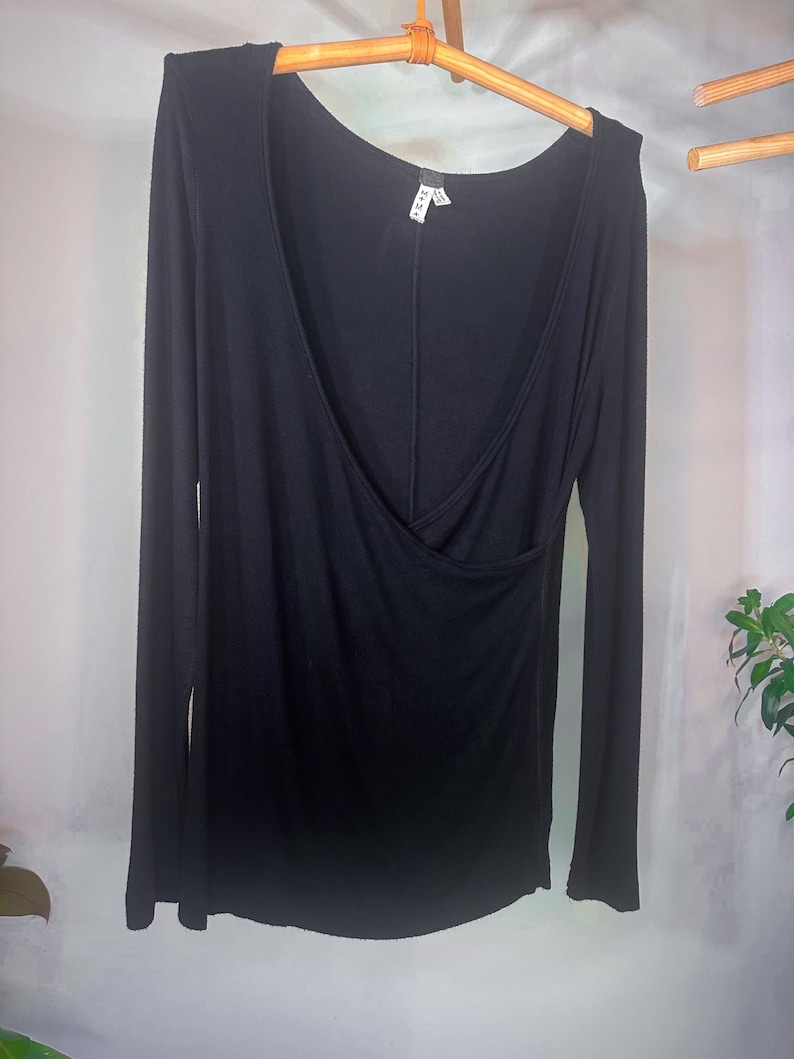 Puede incluir: Una camisa negra de manga larga con cuello en V profundo y dise&ntilde;o de envoltura. La camisa est&aacute; hecha de una tela suave y el&aacute;stica.
