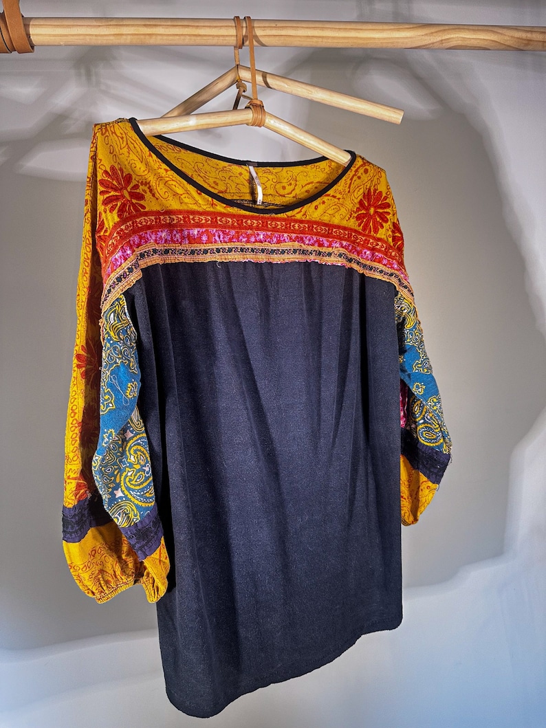 Puede incluir: Una camisa de manga larga con estampado azul y amarillo, con un cuerpo azul oscuro y un ribete colorido alrededor del escote.